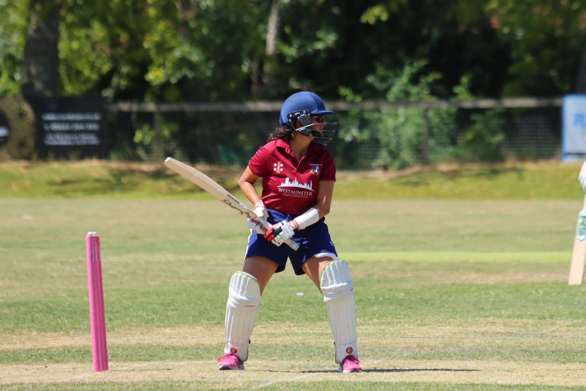 A Tewkesbury batter in a maroon sponsored shirt, watching the ball after playing a shot
