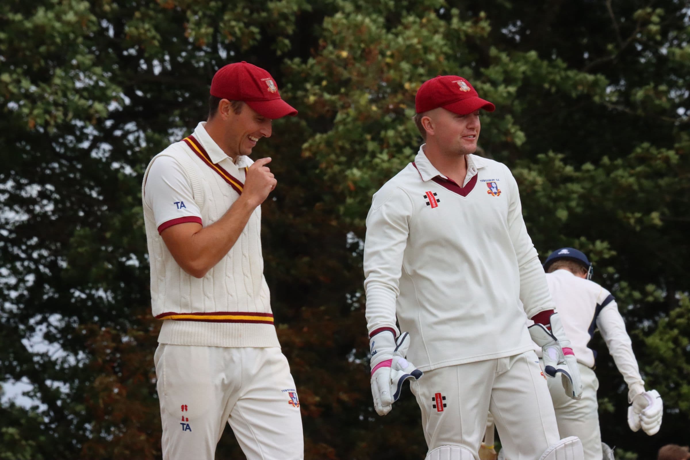Two Tewkesbury players in maroon caps sharing a laugh between overs